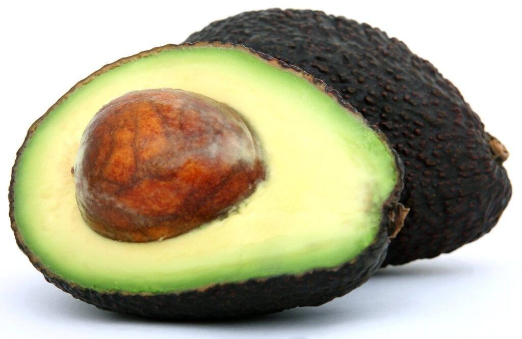 An avocado has been cut in half, and the just-ripened inside is shown facing us, with the pit still intact.