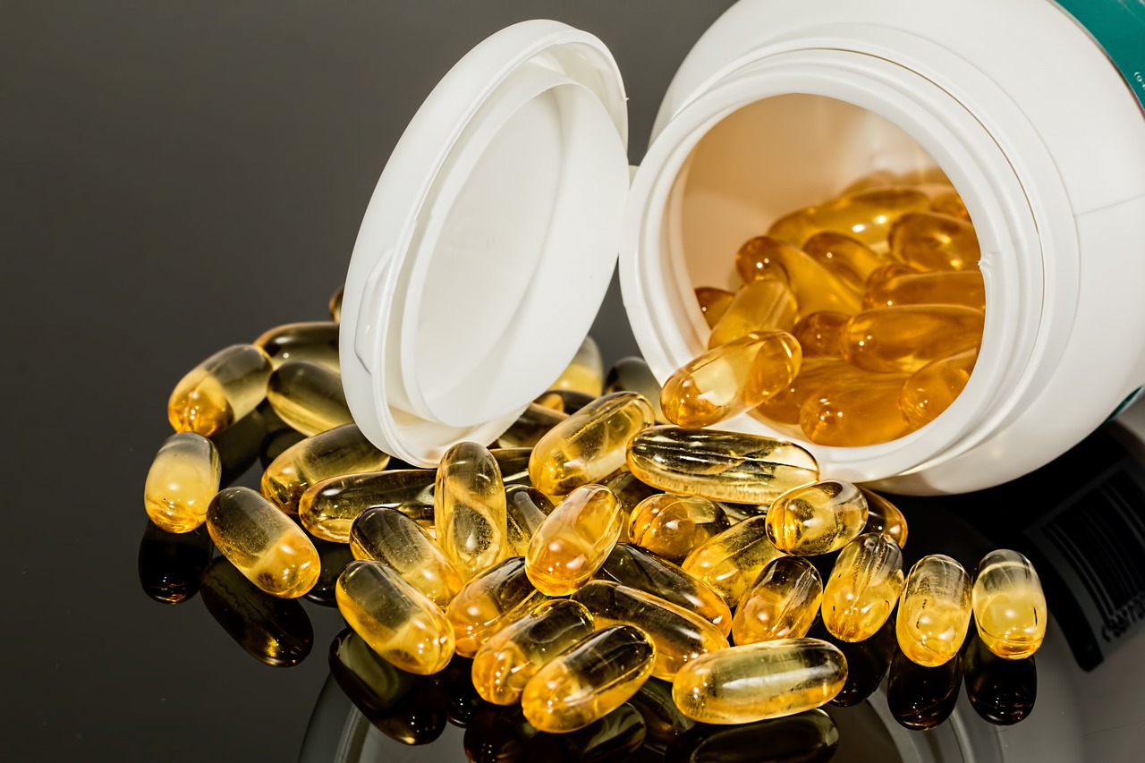 Yellow-clear gel capsules are shown spilling out of a bottle that's on it's side. They would appear to be a supplement of some sort.