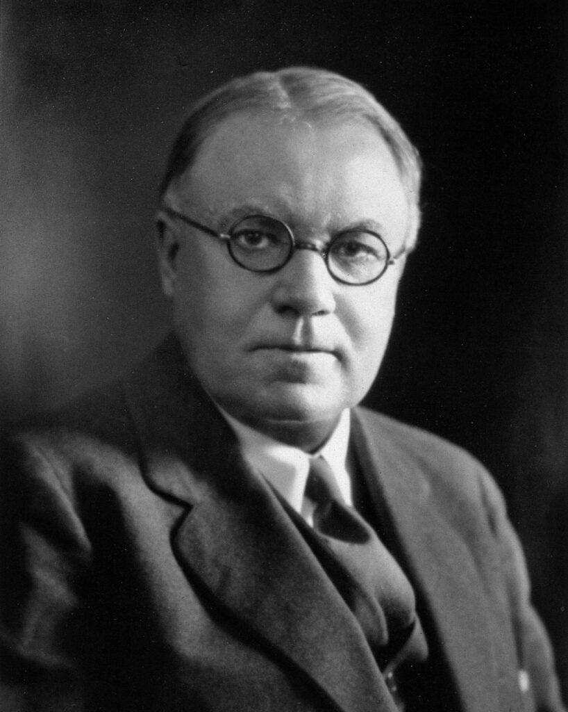 A black and white portrait of Walter Cannon in a suit and tie, glasses on.