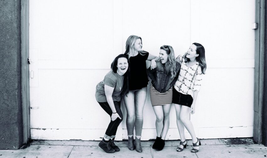 Four young women laughing joyfully in front of a large commercial garage door backdrop.