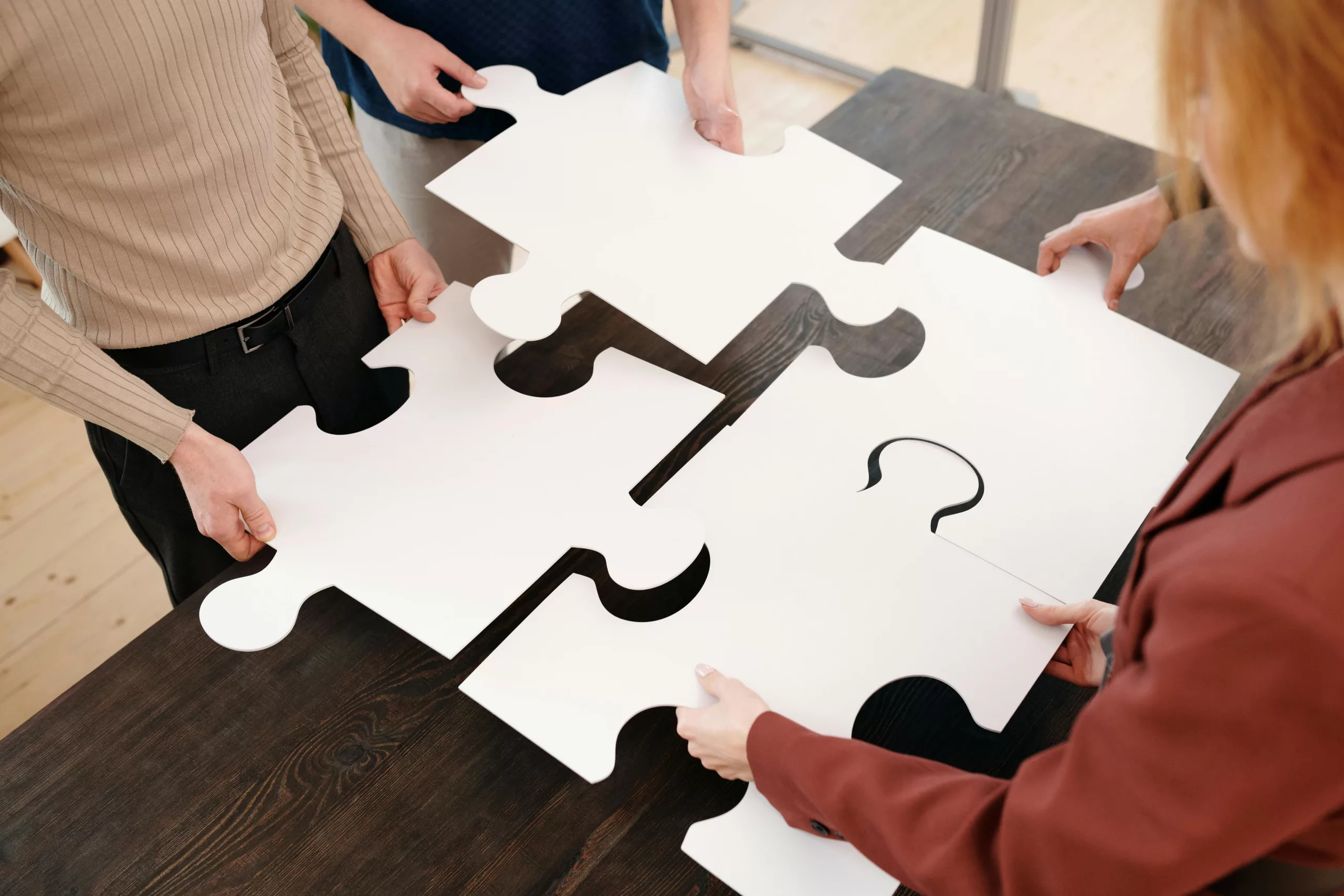 Four people holding large puzzle pieces to form a complete puzzle on a table.